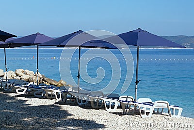 Blue umbrellas and chaise for relax and comfort on sea beach. Happy summer vacations and tourism concept. Paid service on Stock Photo