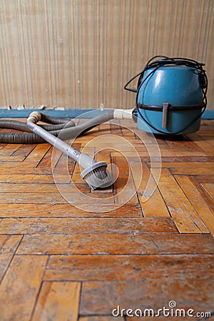 Blue vacuum cleaner stands on shabby parquet floor Stock Photo