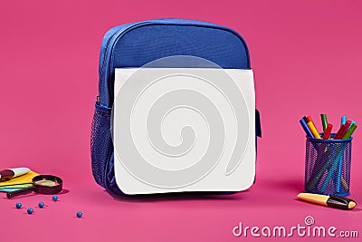 Blue and white school bag, colorful felt-tip pens in a stand, blue pins, magnifying glass and pencil cases on pink Stock Photo