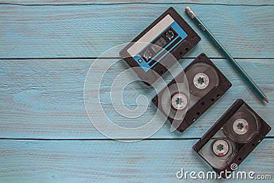 On a blue wooden background, there are three audio cassettes and a pencil. There is a space for text on the left side of the frame Stock Photo