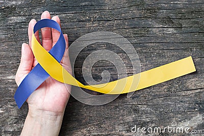 Blue yellow awareness ribbon on helping hand for World down syndrome day WDSD March 21 raising support on patient Stock Photo
