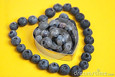 Blueberry heart shape symbol concept for healthy eating and lifestyle. Isolated on yellow background. Stock Photo