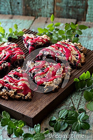 Blueberry scones with raspberry jam topping on oak cutboard with blueberry leaves on old painted wood background Stock Photo