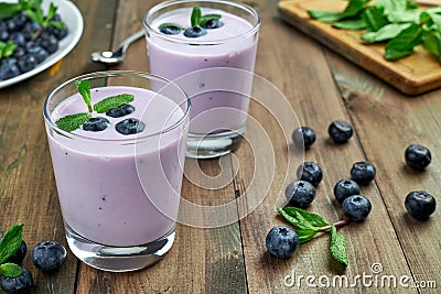 Blueberry yogurt with fresh berries and mint leaves. Two glasses of yogurt and a lot of scattered blueberries Stock Photo