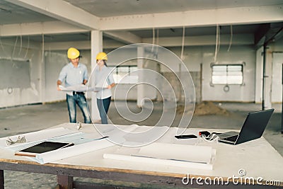 Blueprint, laptop computer, and industrial tools at construction site with two engineers or architects working in background Stock Photo