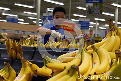 Blur motion of clerk stocking banana on display rack inside superstore produce department Editorial Stock Photo