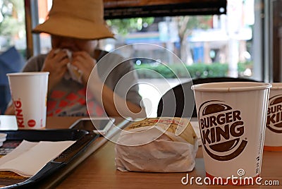 Blur motion of woman eating burger and drinking hot coffee at Burger King fast food restaurant Editorial Stock Photo