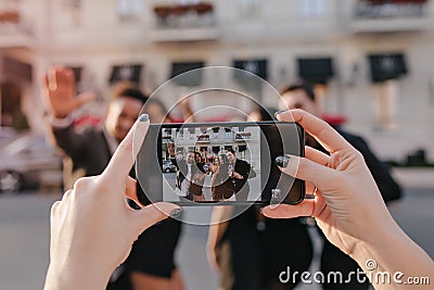 Blur outdoor portrait of girls and boys posing in front of building before party with smartphone in focus. Lady with Stock Photo