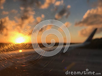 Blurred bright orange sun and the wing of the aircraft during dawn on the runway against the forest silhouette Stock Photo