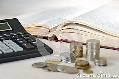 Blurred coins in piles and calculator against background of an open book. Concept of high education costs Stock Photo