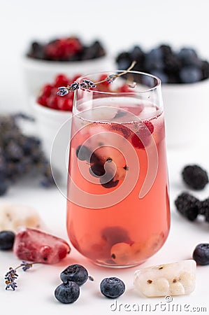 Blurred image of a chilled fruit drink with ice and a sprig of lavender in the foreground, various berries in the background on a Stock Photo