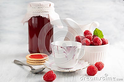 Blurred image of a cup, spoon, plate with raspberries, a jar of raspberry jam and cookies. The concept of canning Stock Photo