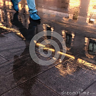 Blurred reflection of a historic building in a puddle, silhouette of a man in the wet sidewalk. Rain in the city at Stock Photo