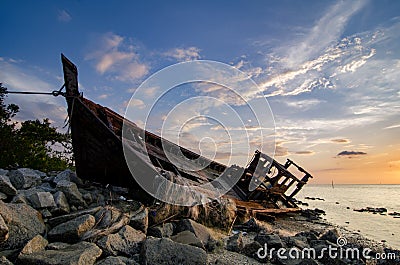 Silhouette image of abandon shipwrecked on rocky shoreline. dark cloud and soft on water Stock Photo