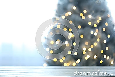 Blurred view of beautiful Christmas tree with yellow lights near window indoors, focus on wooden table Stock Photo