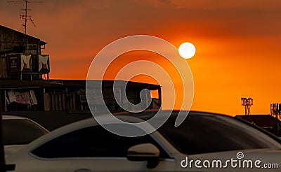 Blurred white Car driving on the road near slum community at sunset with beautiful orange sunset sky. Traffic jam in town while Stock Photo