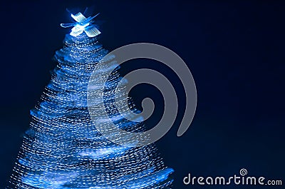Blurry creative lighted christmas tree in monochrome classic blue palette on a dark background in trendy color of 2020. Xmas and Stock Photo