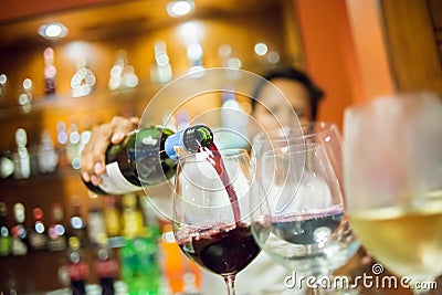 Blurry Man pouring red wine into glass with white wine foreground, selective focus. Stock Photo