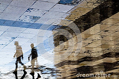 Blurry reflection shadow silhouettes of two young men walking on a vintage pavement on wet city street Stock Photo