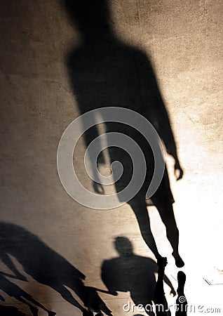 Blurry silhouette shadow of one young woman and family with children walking behind her Stock Photo