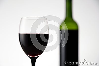 Blurry view of glass of red wine with bottle in the background. Wineglass full of alcohol drink on white background Stock Photo