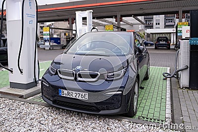 BMW i3 electric car is being charged from an electric charging station, charging cable, another gas station for traditional Editorial Stock Photo