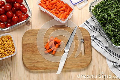 Board with baby carrots, knife and containers with fresh products on wooden table, flat lay. Food storage Stock Photo