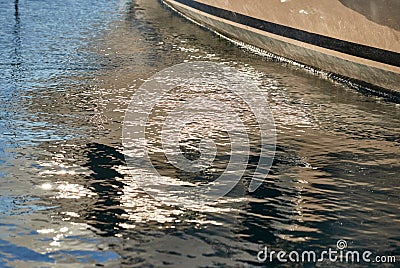 Board of the big boat of gold color, golden reflections of the sun on water at sunset, interesting texture, smooth lines Stock Photo