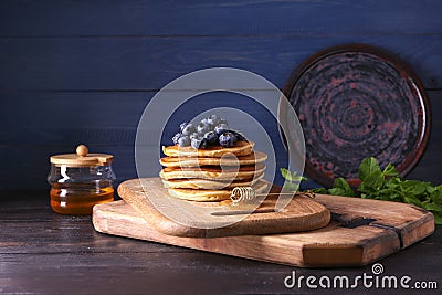 Board with tasty pancakes, honey dipper and blueberries on wooden table Stock Photo