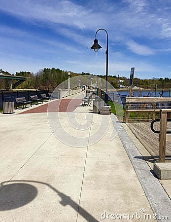 Boardwalk with lamp pole and shadow and boats in harbor Stock Photo