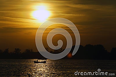 Boat on a calm river at sunset with sunlight reflecting on water Stock Photo