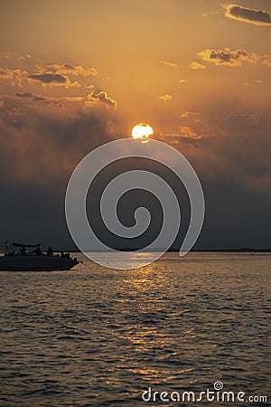 Boat on ocean, Bright sun in an orange sky with dark clouds at sunset Stock Photo