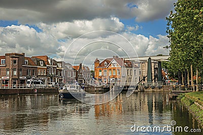 Boat passing by bascule bridge raised on tree-lined wide canal in cloudy day at Weesp. Editorial Stock Photo