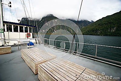 Boat sailing along mysterial coastline with steep rocky and lush vegetation mountains topped with foggy sky Stock Photo