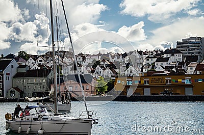 Boat sailing on the sea in the foreground with picturesque houses in the background in Stavanger marina port Editorial Stock Photo