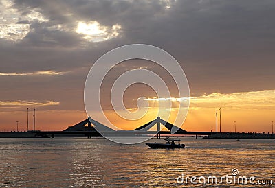 A boat sailing during sunset with Sheikh Isa Bin Salman causeway Bridge at the backdrop Stock Photo