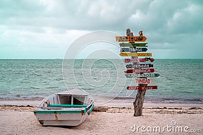 Boat on a sandy beach with directions signs on a trunk and the Caribbean sea in the background Editorial Stock Photo