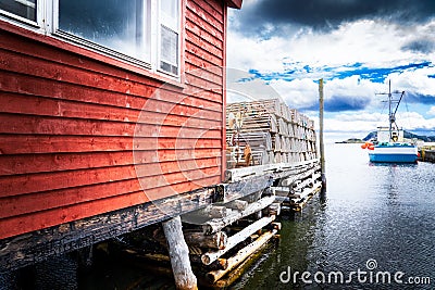 Boat shed and dock loaded with lobster traps overlooking a small harbour with fishing boats near Trinity Newfoundland Stock Photo