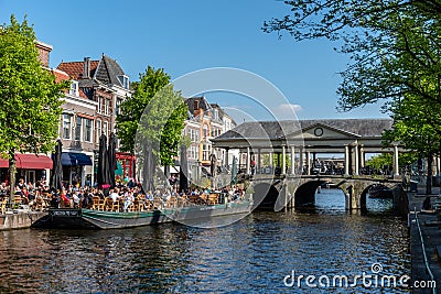 Boat terrace full of people enjoying the sun, food and drinks in the canal of the old town center of Leiden. Bridge Editorial Stock Photo