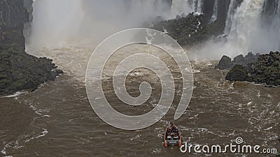 A boat with tourists sails along a raging river with rocky steep banks to a waterfall. Stock Photo