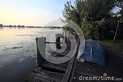 Boat on a wooden pier by the lakeshore next to reeds at sunset Stock Photo