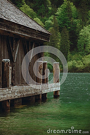 Boathouse sitting in the middle of the water next to wooden beams in Berchtesgaden Stock Photo