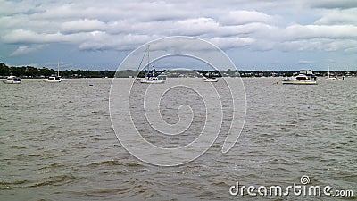 Boats anchoring in a bay on a cloudy morning. Coastal village in the far distance. Stock Photo
