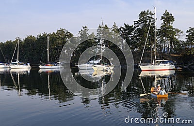 Boats shore tied in Princess Bay with couple rowing dinghy, Wallace Island, Gulf Islands, British Columbia Editorial Stock Photo