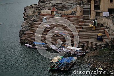 Boats and a small pedestrian bridge on the ghats of narmada river in the holy city of omkareshwar madhya pradesh India Editorial Stock Photo