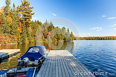 Boats tied up to wooden jetty on a lake with forested shores at the peak of fall foliage on a sunny day Stock Photo