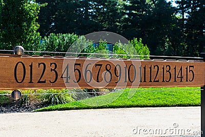 Bocce ball scoreboard. Petanque scoreboard. Black numbers on on brown wooden plank. Green outdoors landscape background Stock Photo