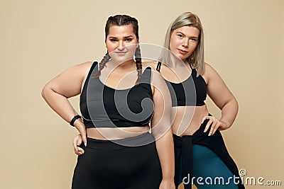 Body Positive. Plus Size Models Portrait. Blonde And Brunette Women In Sport Clothes On Beige Background. Stock Photo