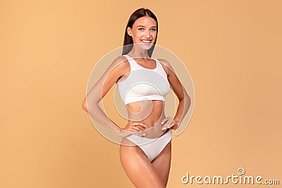 Body slimming concept. Happy lady with slim figure in white underwear smiling at camera over beige studio background Stock Photo