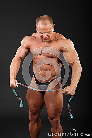 Bodybuilder holds measuring tape and looks down Stock Photo